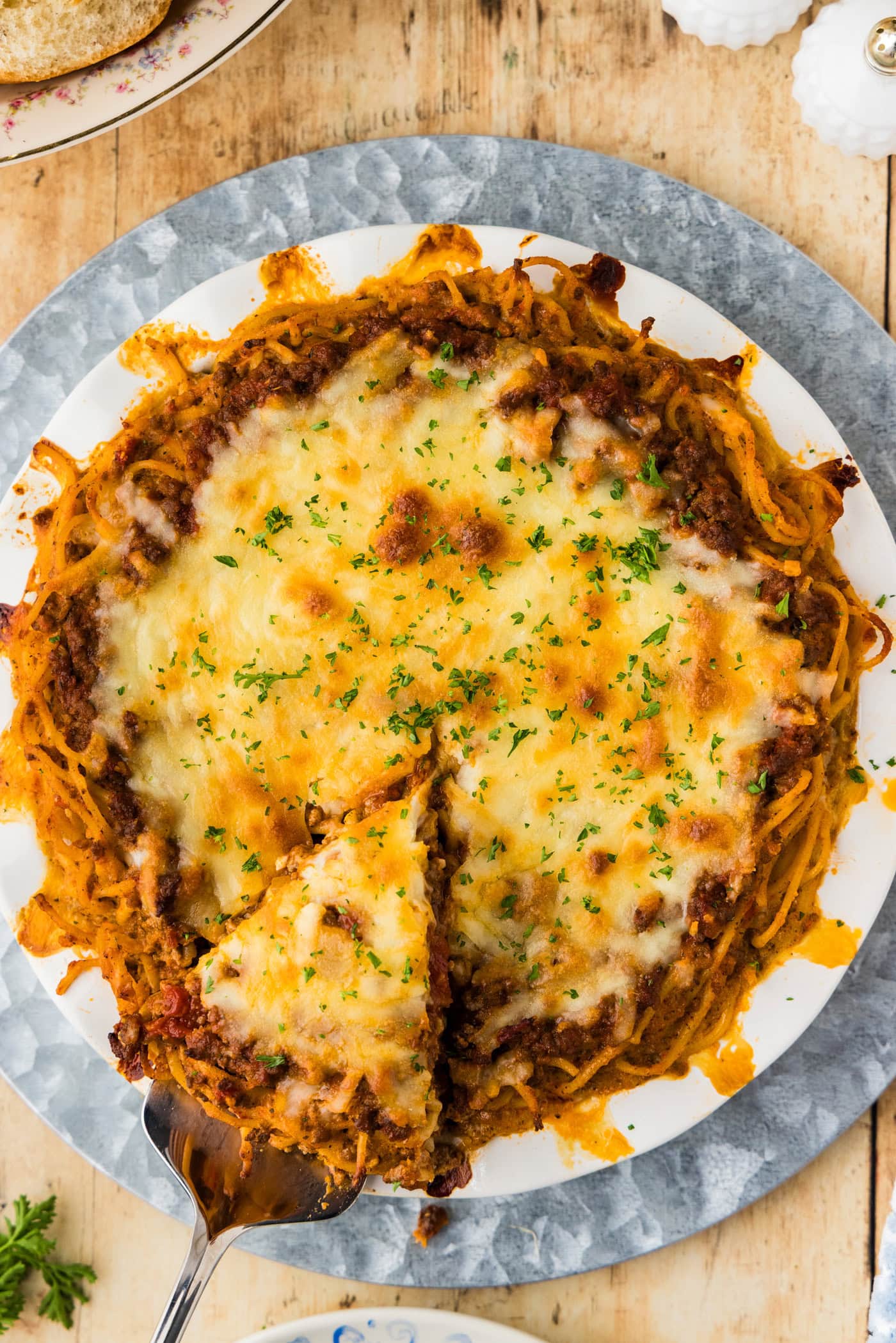 Overhead spaghetti pie with one slice cut and lifted out on a pie server