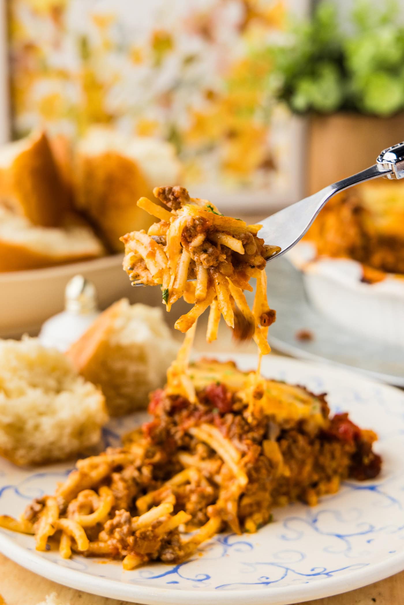 Forkful of spaghetti pie lifted from a slice showing melted cheese and meat sauce