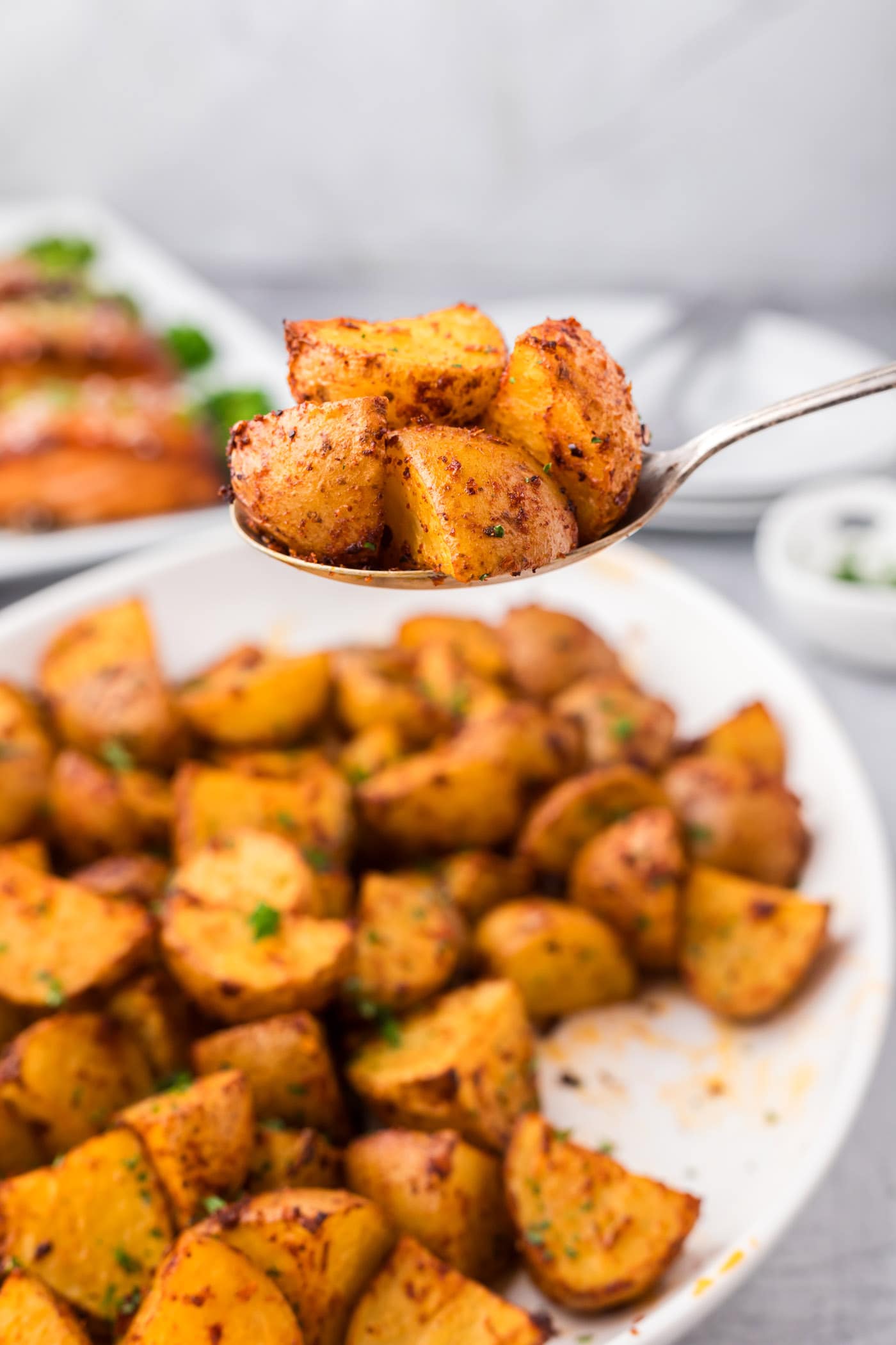 Spoonful of Spicy Potatoes held above a platter of Spicy Potatoes