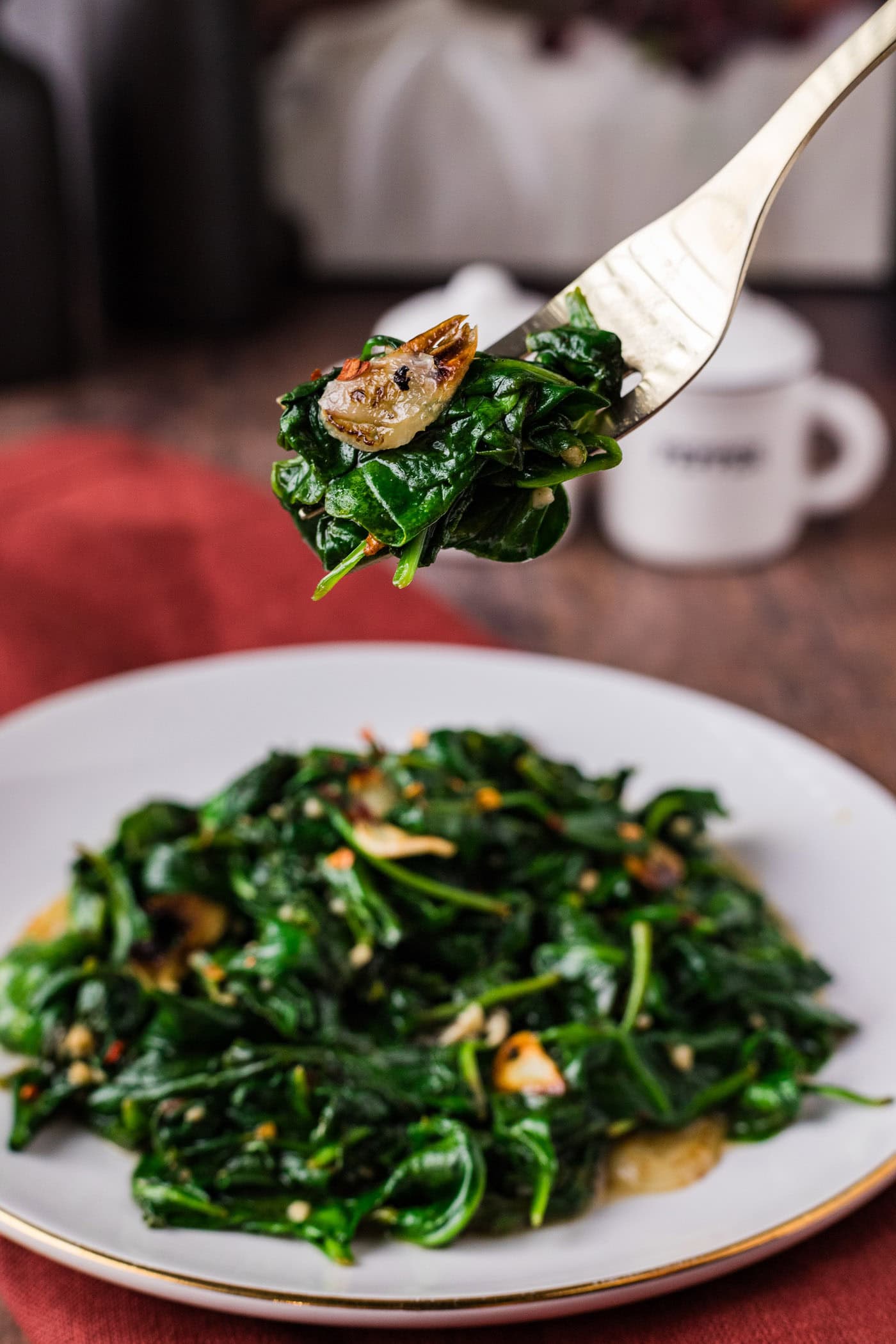 Fork of Stir Fried Spinach held above a plate of Stir Fried Spinach