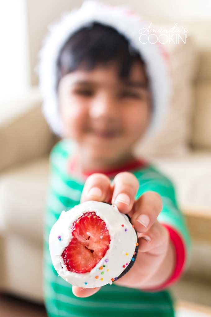 little boy holding out a chocolate covered strawberry with a bite out of it