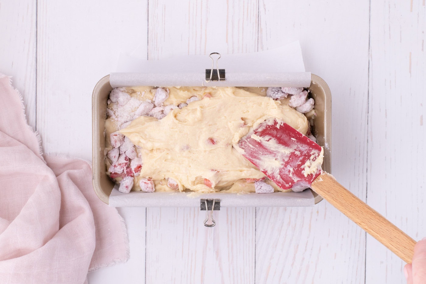 spreading strawberry batter over diced strawberries in a loaf pan