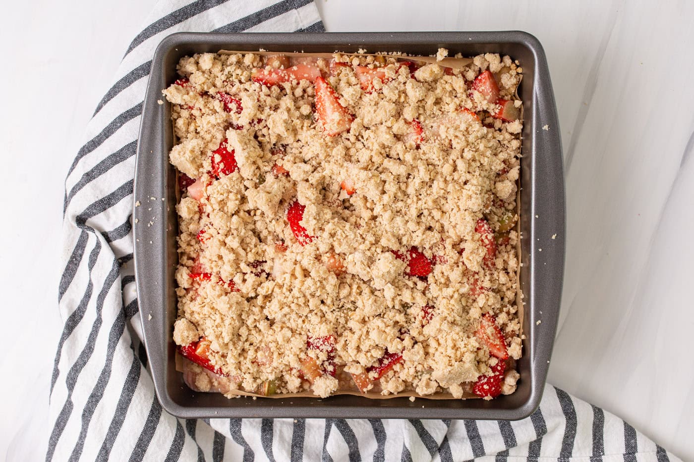 crumble topping over strawberry rhubarb crumble bars in a pan