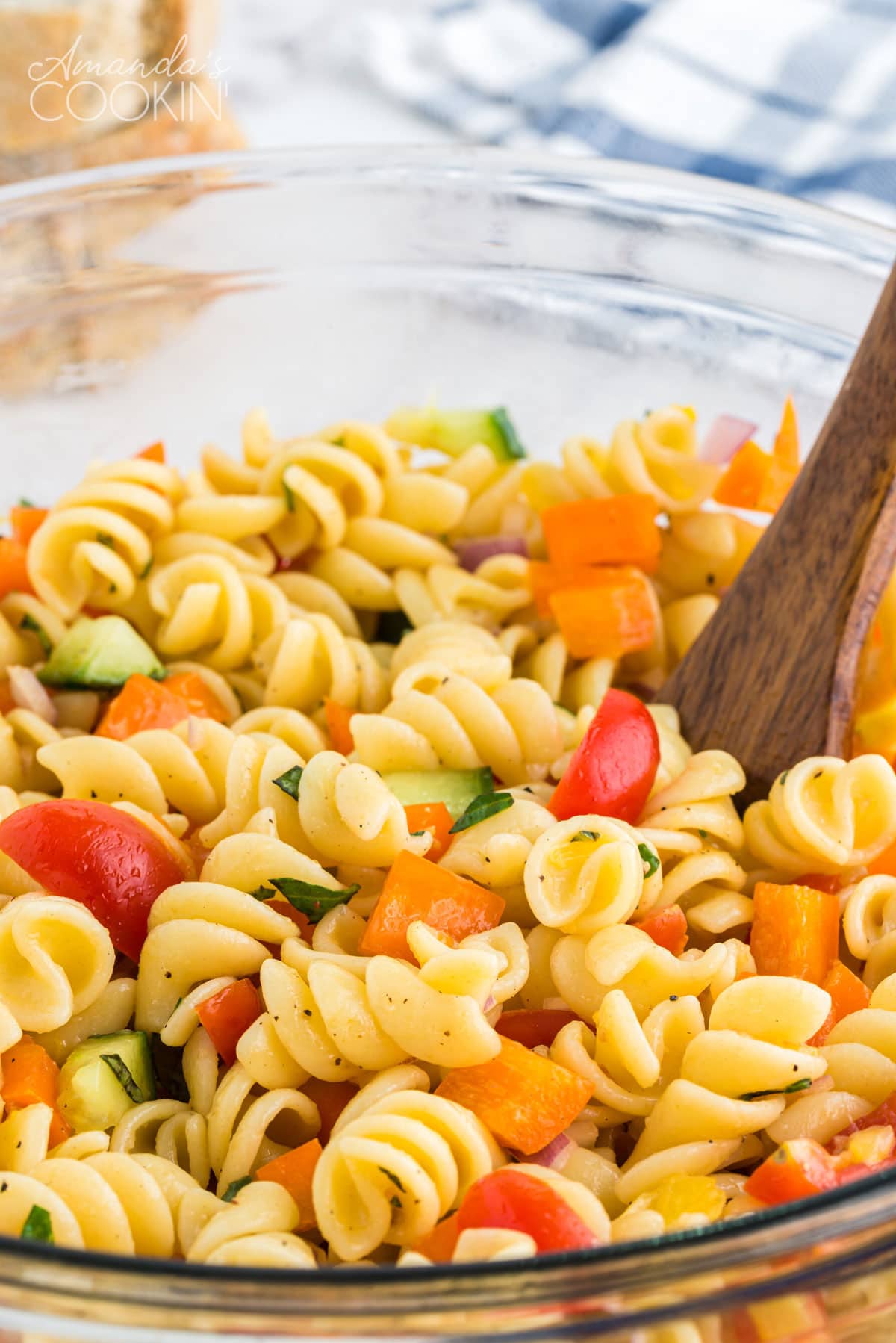 close up of summer pasta salad in a bowl with a wooden spoon