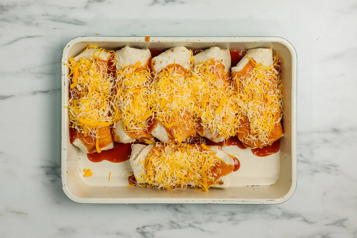 enchiritos in a baking pan topped with enchilada sauce and cheddar cheese