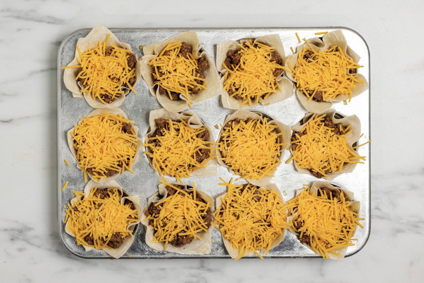 final layer of shredded cheese on top of taco cups in a muffin pan