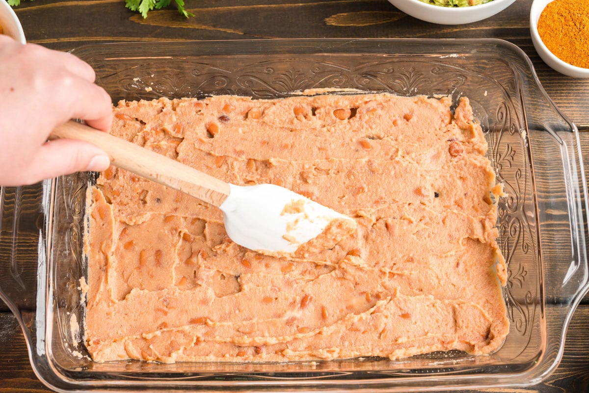 spreading refried beans in a glass pan