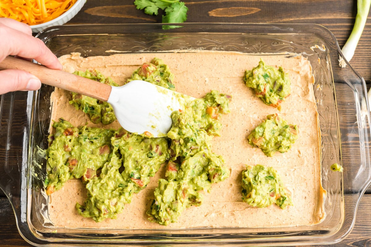spreading guacamole over sour cream mixture on pan