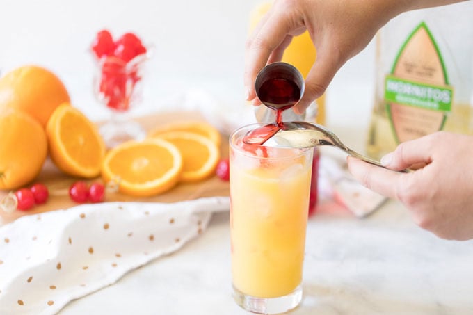 pouring grenadine syrup over the back of a spoon into tequila sunrise glass