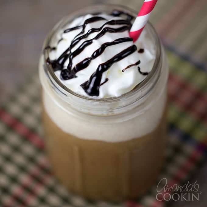 An overhead shot of a mason jar filled with a mocha Frappucino topped with whipped cream, chocolate sauce and a red and white stripped straw.