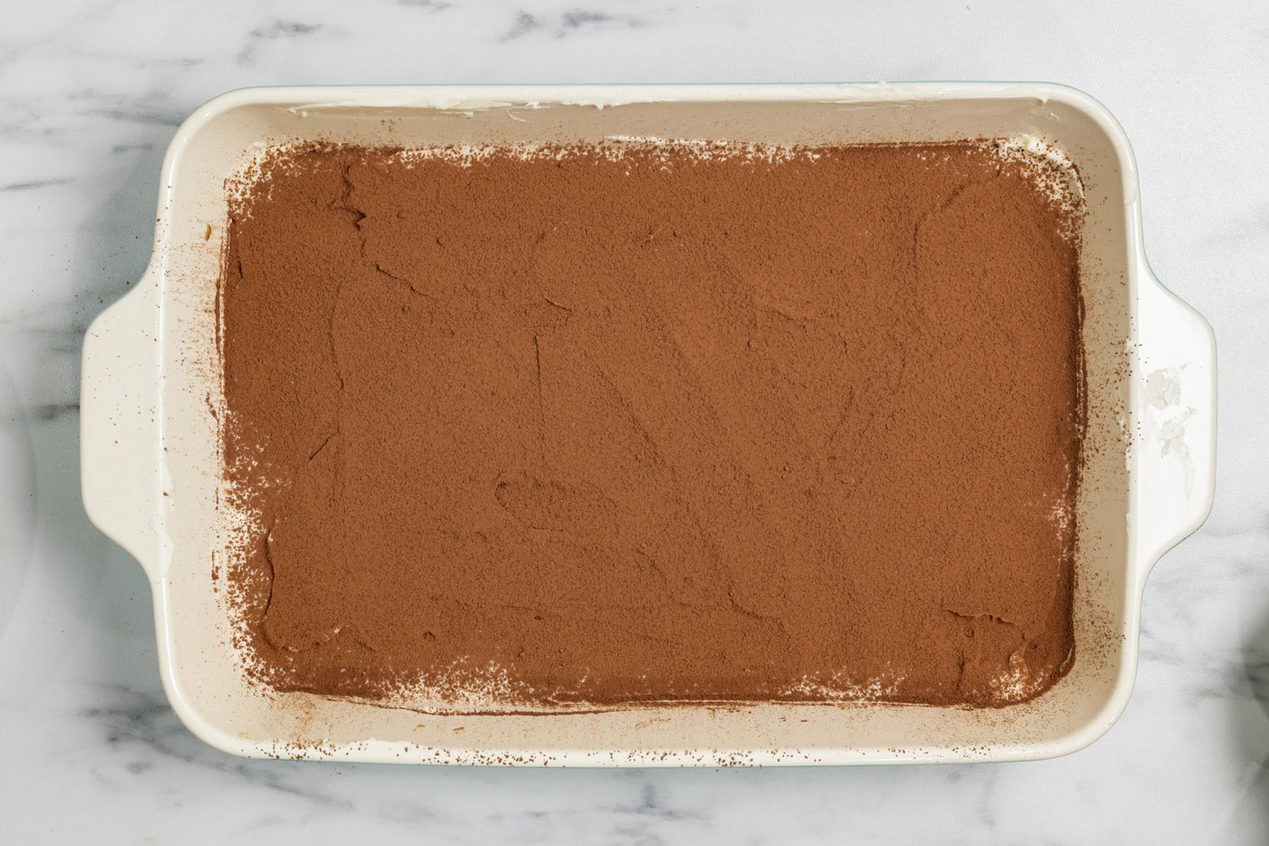 cocoa powder dusted over mascarpone mixture in a baking dish