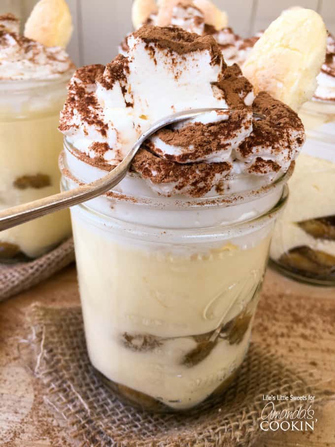 A close up photo of a tiramisu trifle in a mason jars with a spoon.