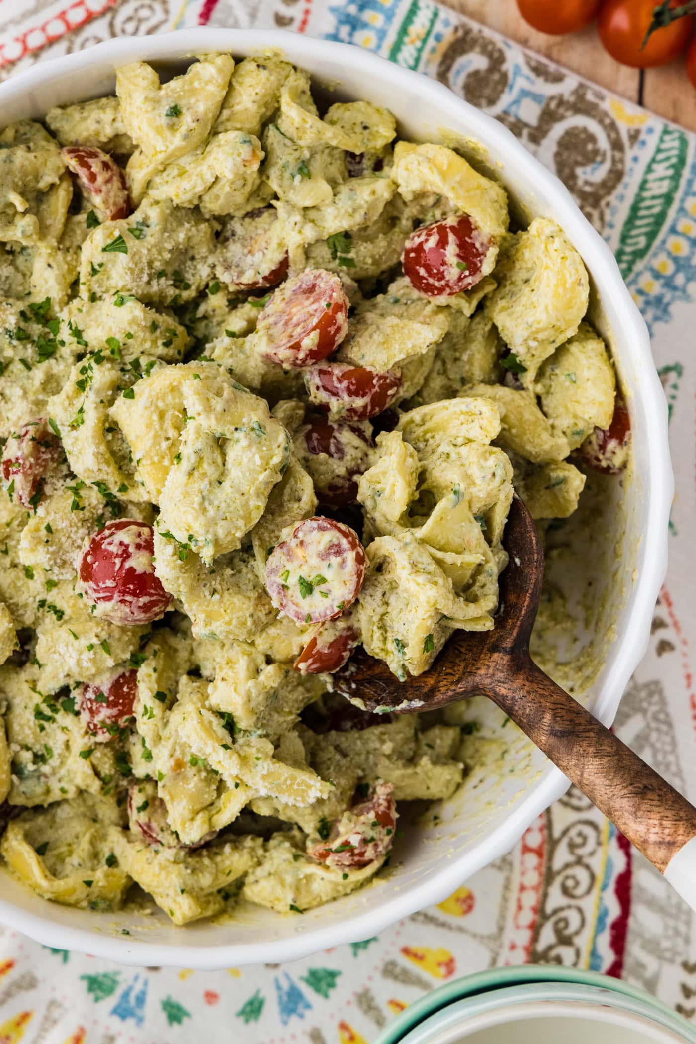 creamy tortellini pesto pasta salad in a serving bowl with a wooden spoon