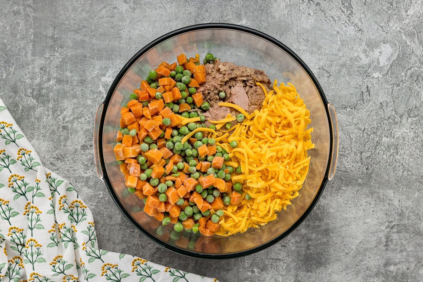 frozen peas and carrots with shredded cheese and tuna in a bowl