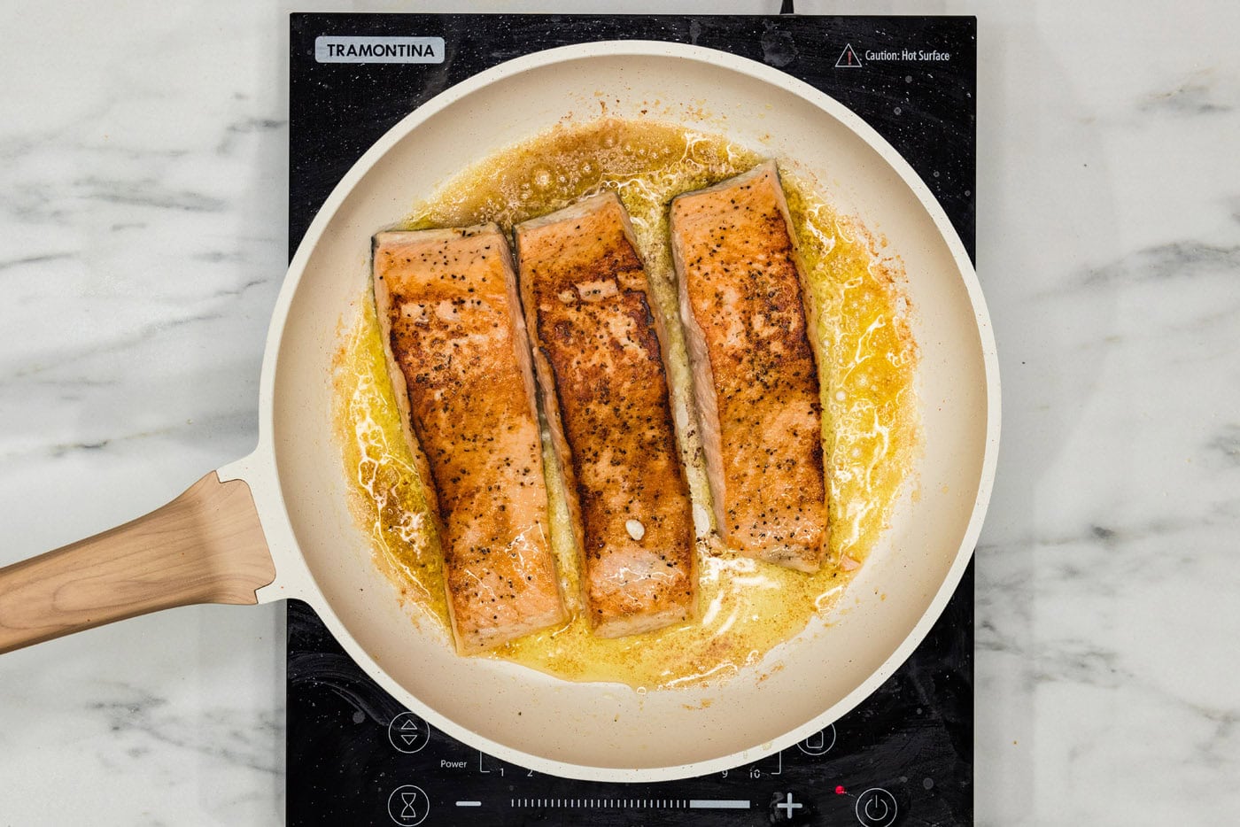 salmon filets cooking in a skillet with oil and butter