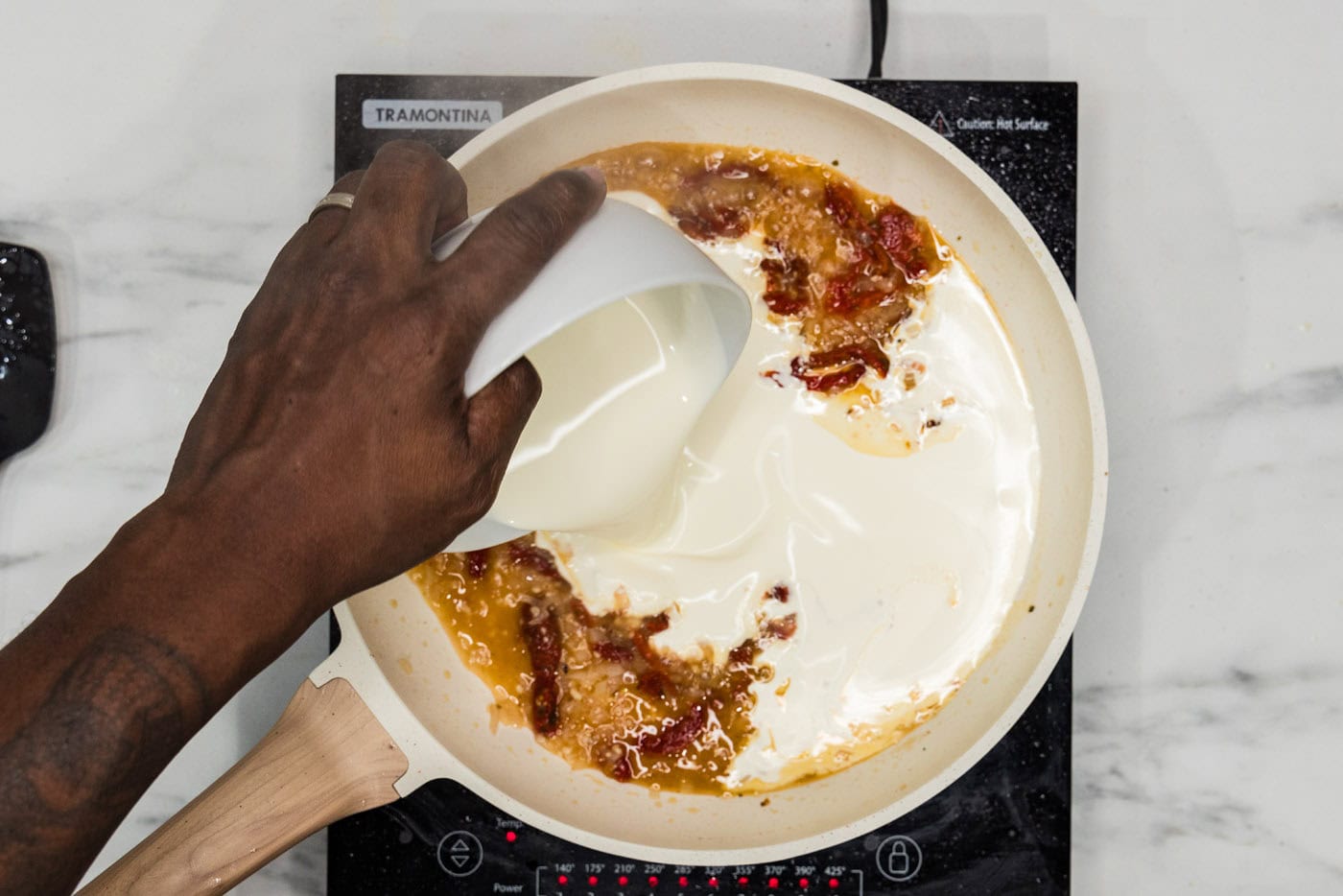 pouring heavy whipping cream into sauce mixture with sun dried tomatoes