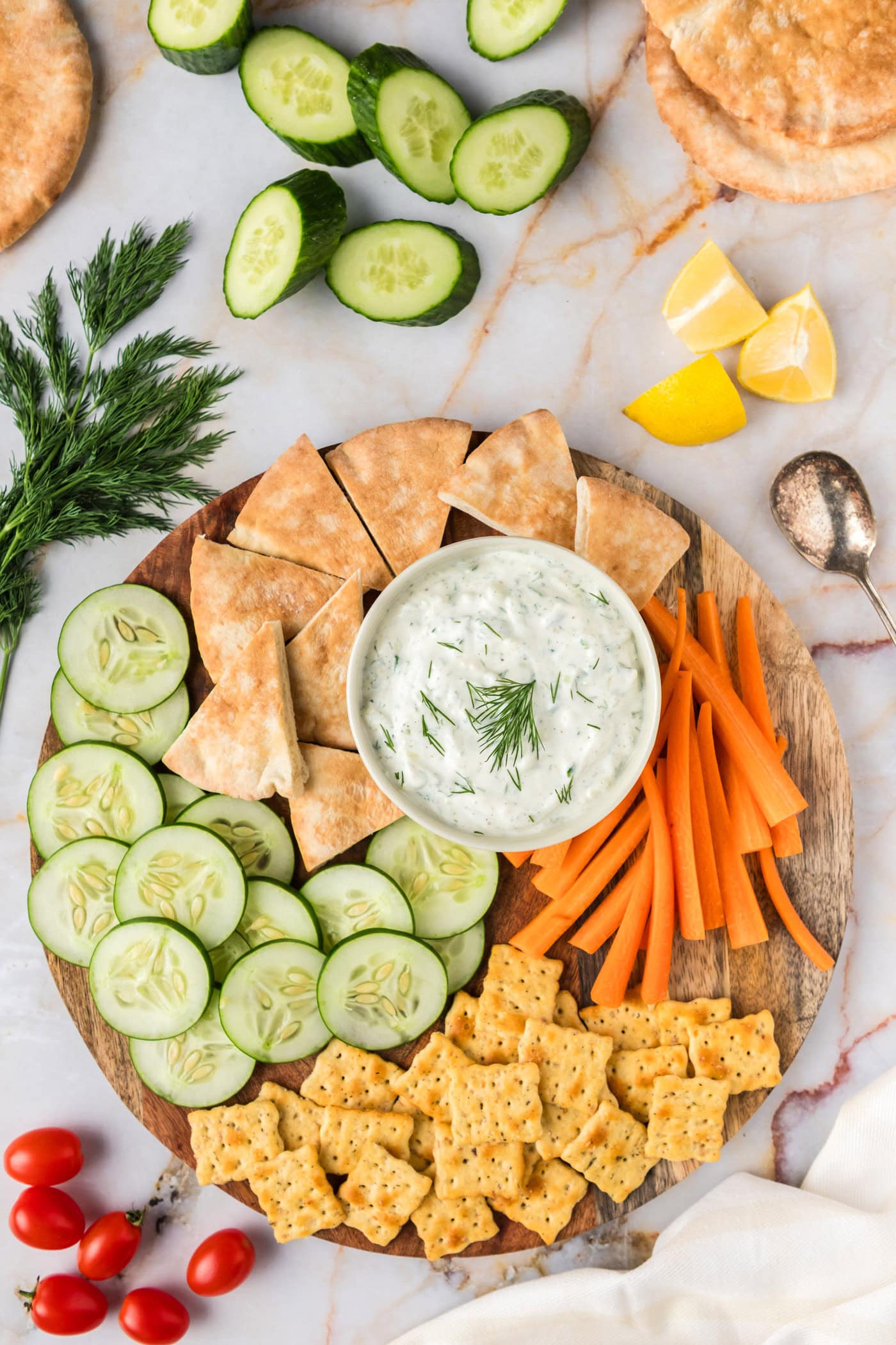 Tzatziki Sauce in a bowl on a platter with pita bread, crackers, carrots and cucumbers