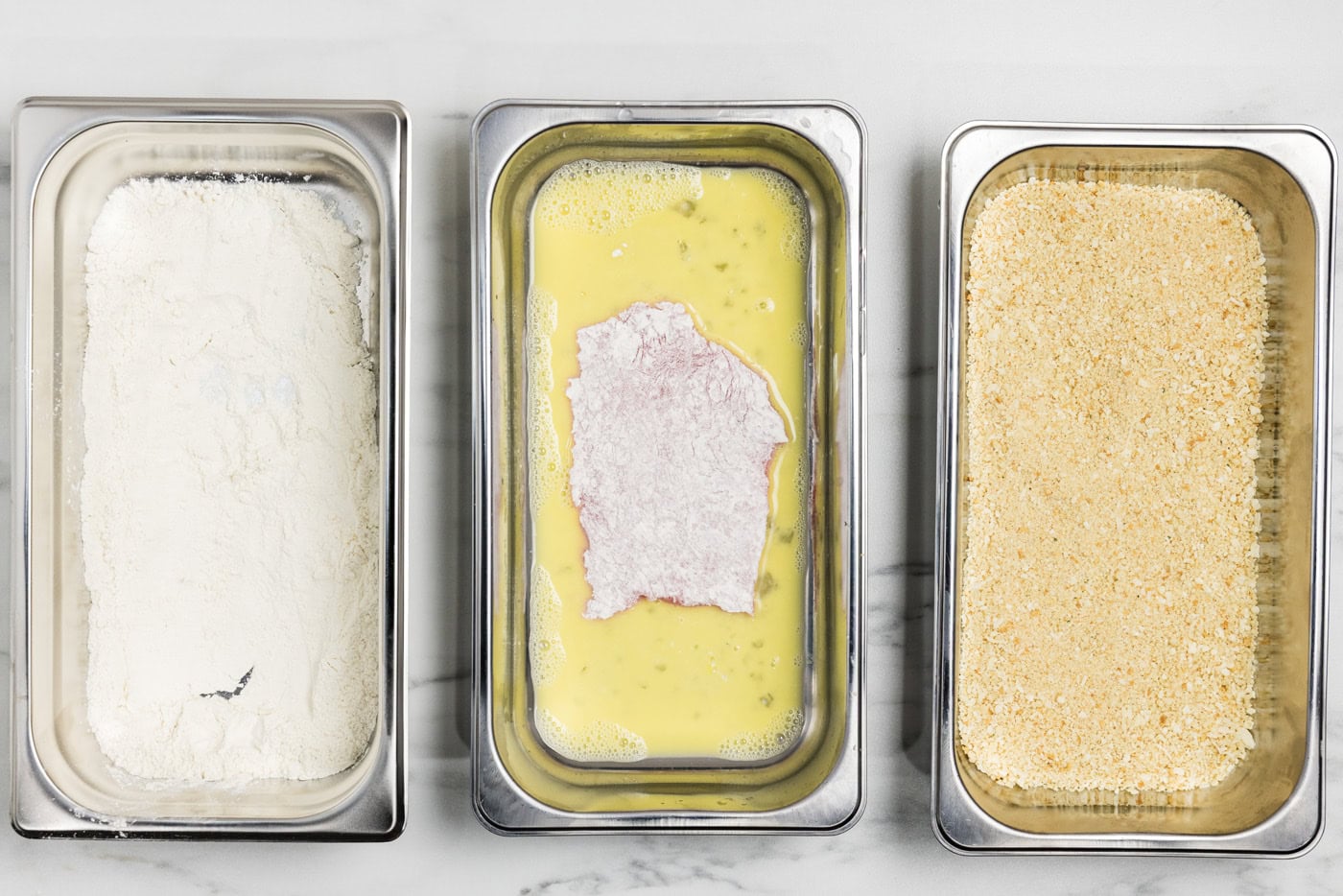 floured veal cutlets in breading tray with egg