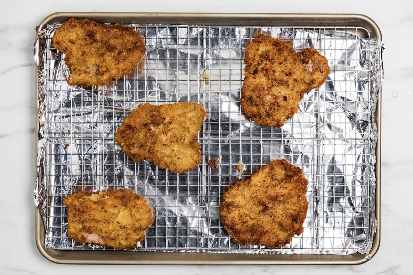 cooked breaded veal cutlets on a wire rack over a baking sheet