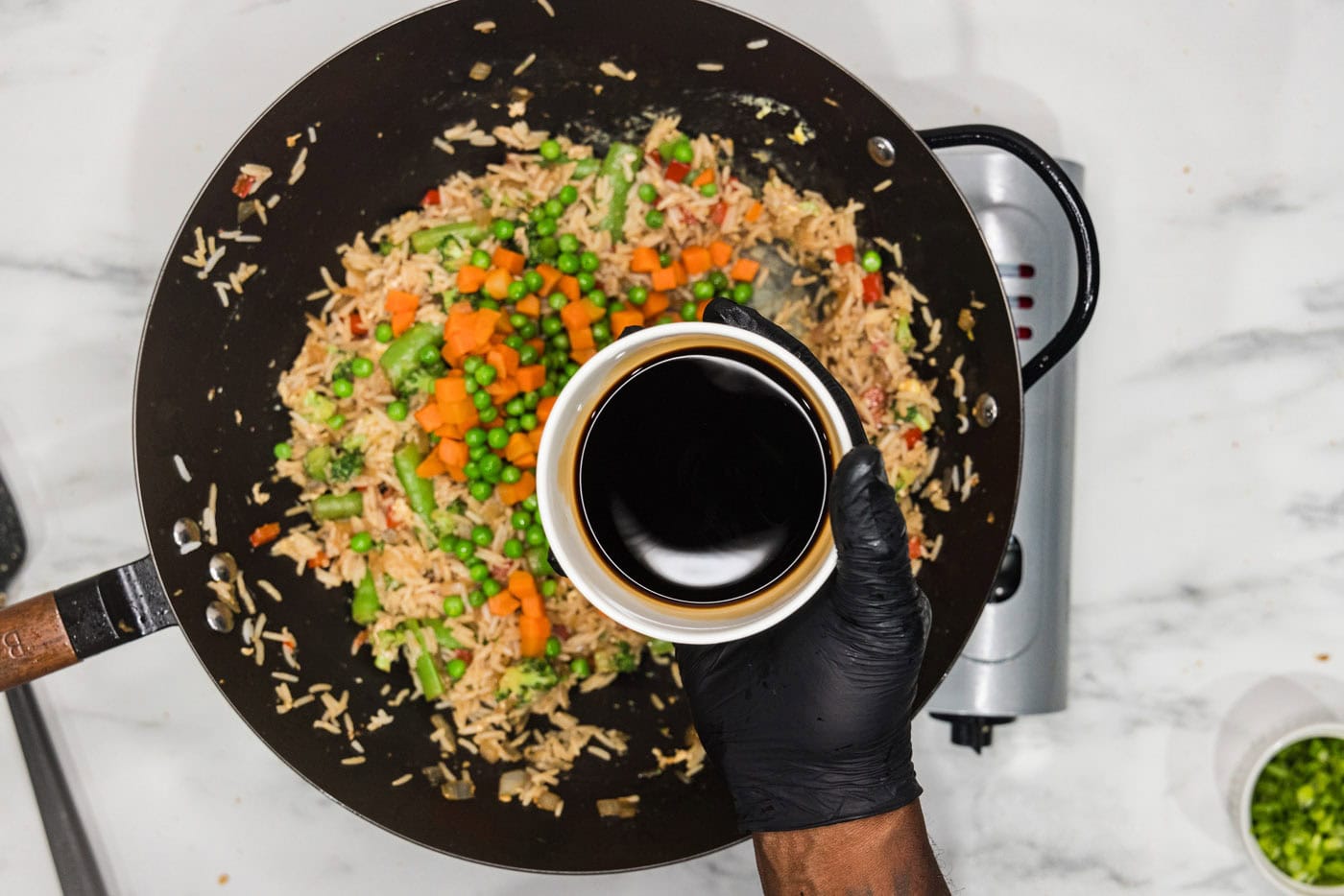 adding soy sauce to wok with vegetable fried rice