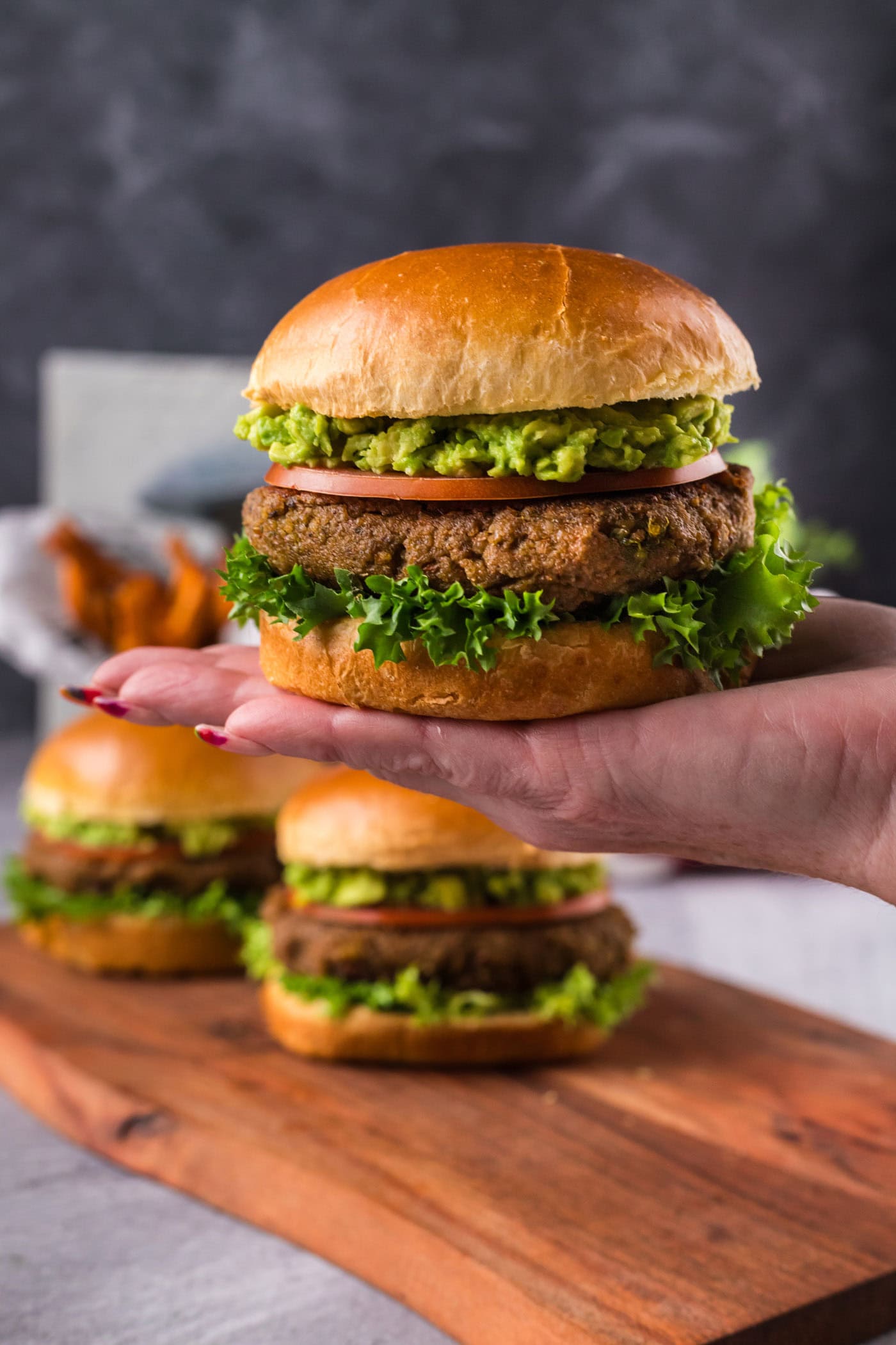 Hand holding up a Veggie Burger with two more on a platter in the background