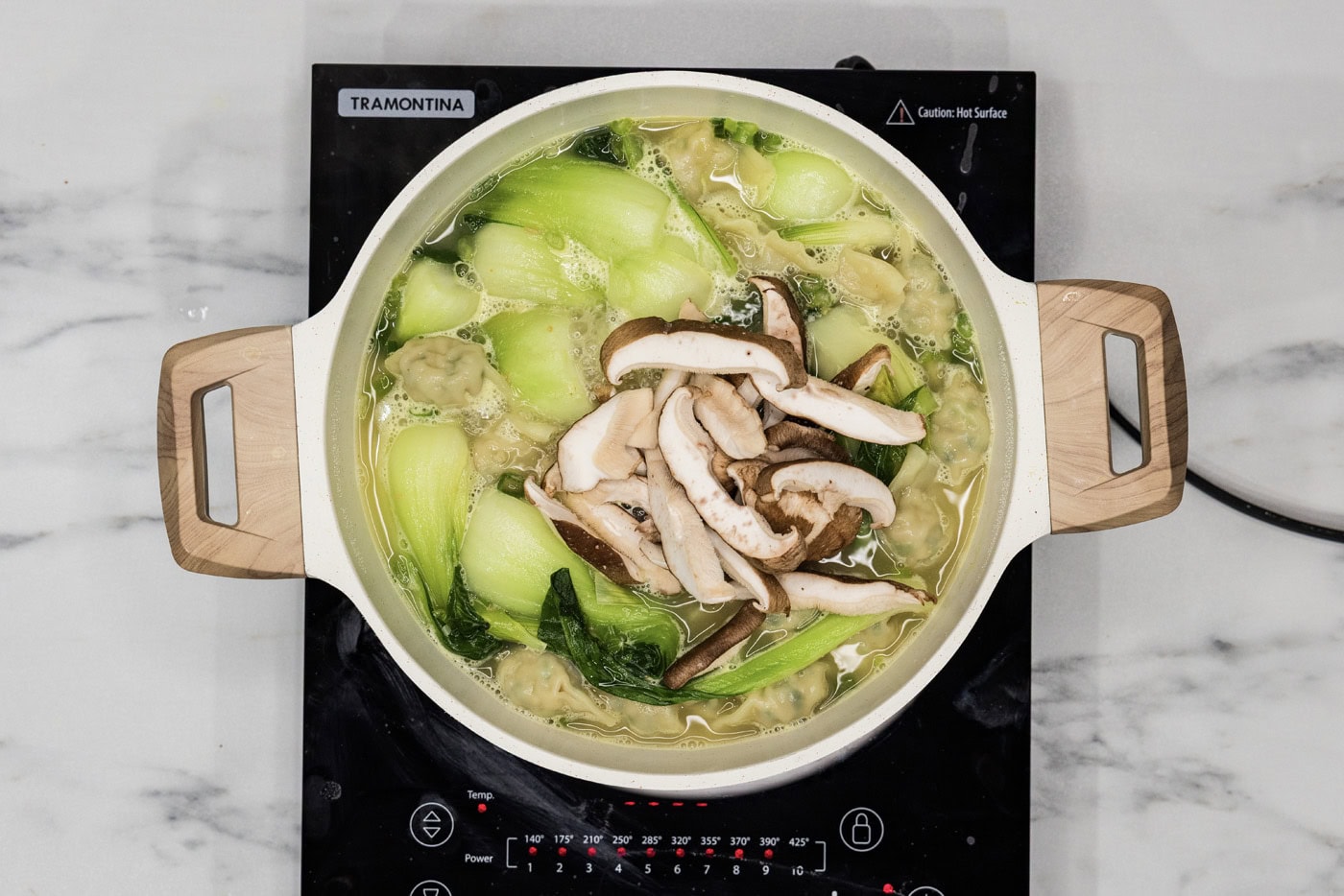 sliced shiitake mushrooms added to stockpot of wonton soup