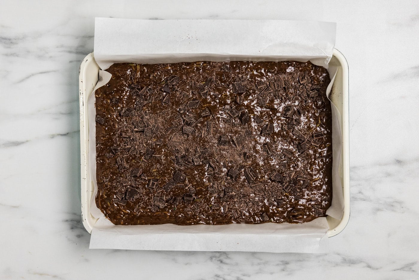 zucchini brownie batter in a pan with chopped chocolate sprinkled on top