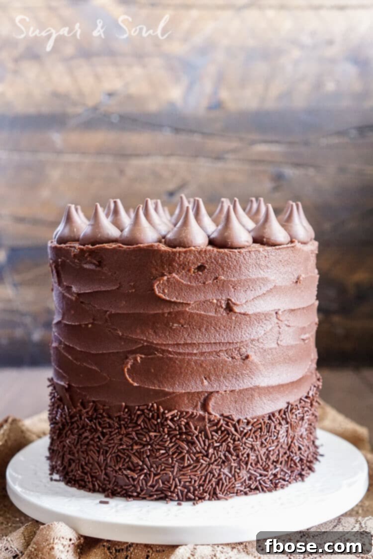 Tall, five-layered Chocolate Pumpkin Cake frosted with creamy chocolate buttercream, adorned with sprinkles and Hershey's Kisses, perfect for fall celebrations.