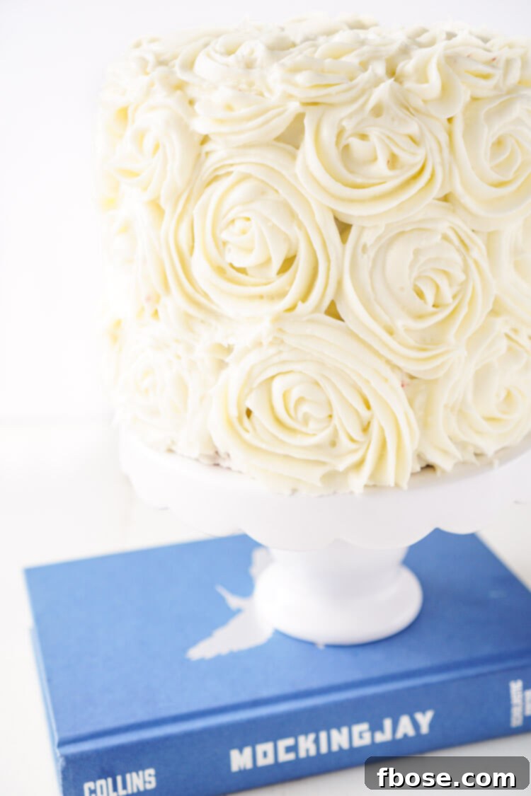 A stunning multi-layered Red Velvet Cake, intricately frosted with white cream cheese roses, paying homage to the complex symbolism in The Hunger Games.