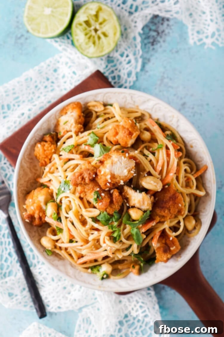 A vibrant platter of Crispy Chicken Thai Peanut Noodles, garnished with fresh cilantro and lime.