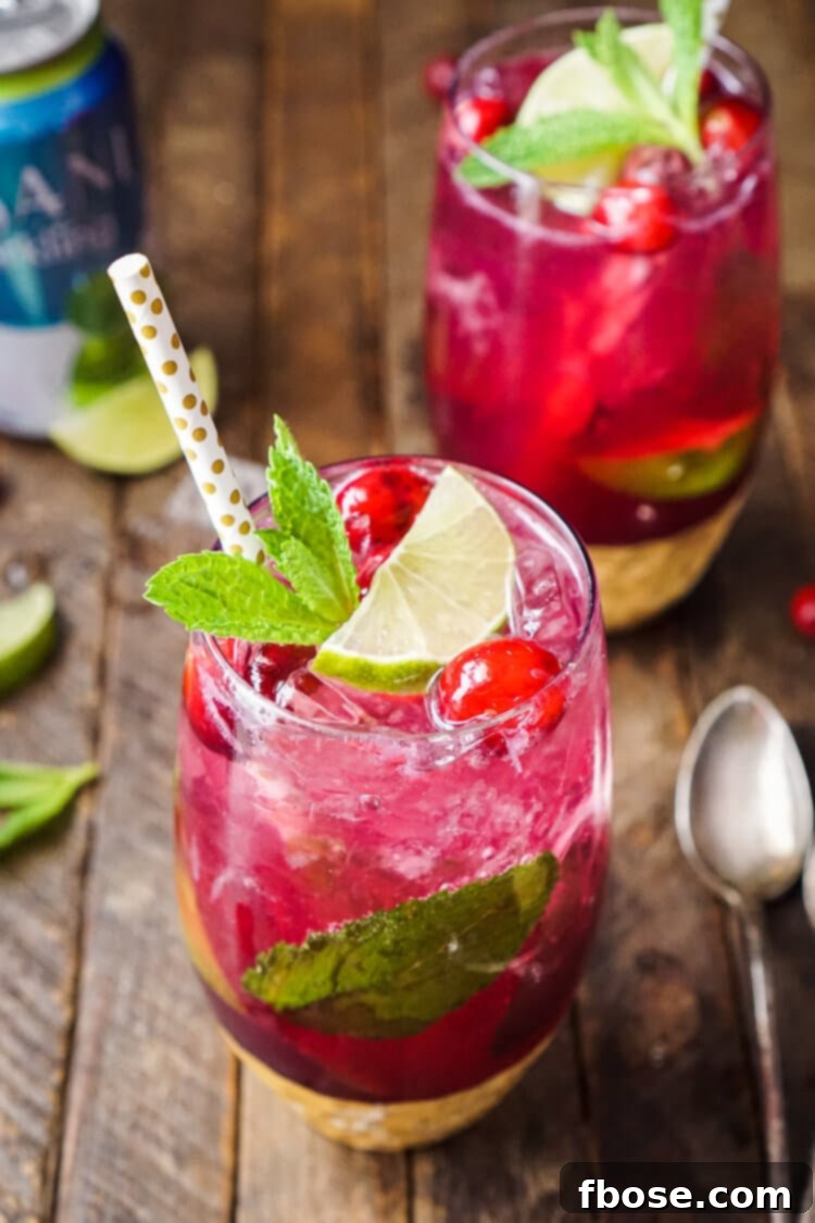 A glass of cranberry mojito on a wooden table, vibrant red with mint and lime garnish.