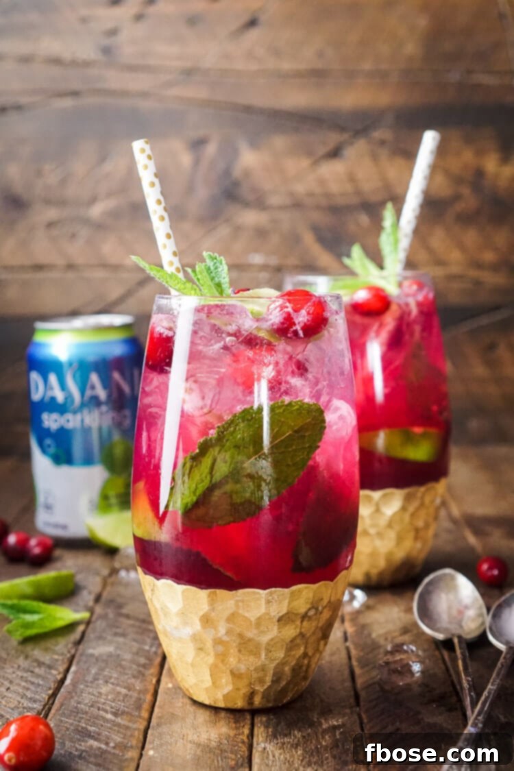 Two glasses filled with cranberry mojito punch on a wooden table, garnished with lime and mint.