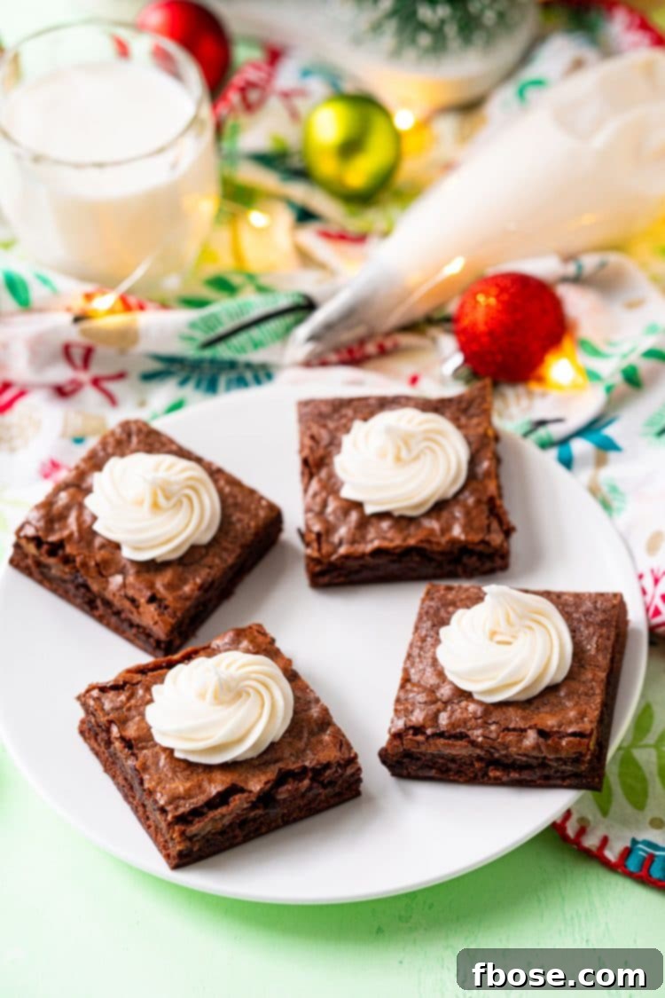 Brownies on a white plate with swirls of buttercream frosting on them and holiday decorations scattered around.