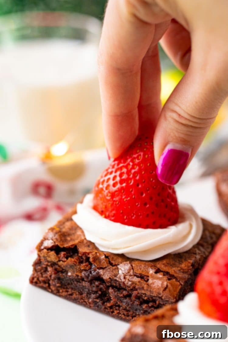 A woman's hand placing a strawberry on top of a frosted brownie.