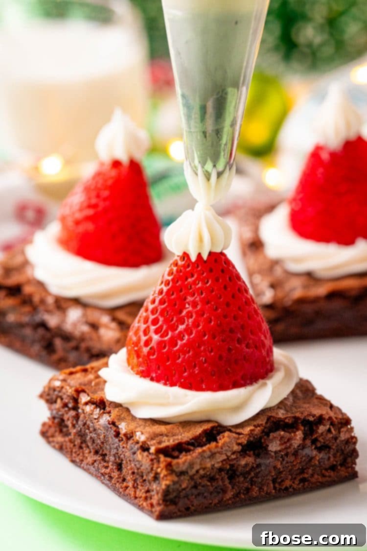 Buttercream frosting being piped onto the top of a strawberry on a brownie to make a santa hat.