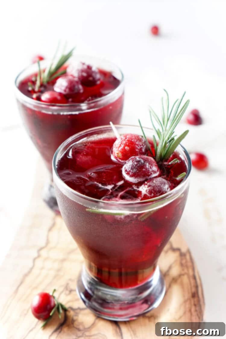 A vibrant Cranberry Cooler mocktail, garnished with sugared cranberries and a sprig of fresh rosemary, set against a festive backdrop. The drink is a refreshing blend of tart cranberries and a hint of mint, perfect for holiday gatherings.