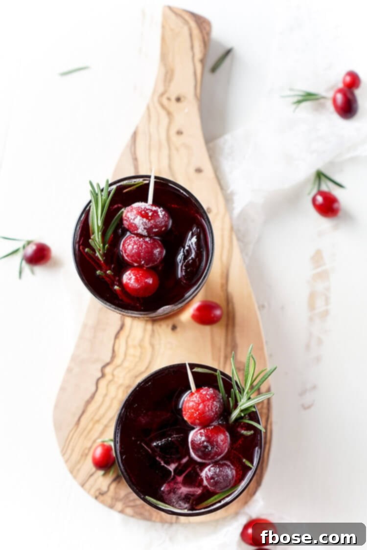 A perfectly garnished Cranberry Cooler mocktail in an elegant glass, featuring sugared cranberries and a sprig of fresh rosemary, ready to be enjoyed as a festive holiday drink.