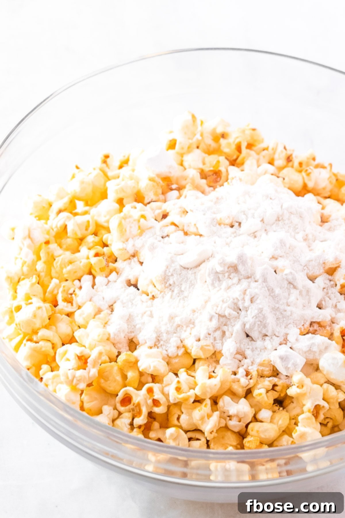 Popcorn and dry cake mix being stirred together in a large glass mixing bowl.