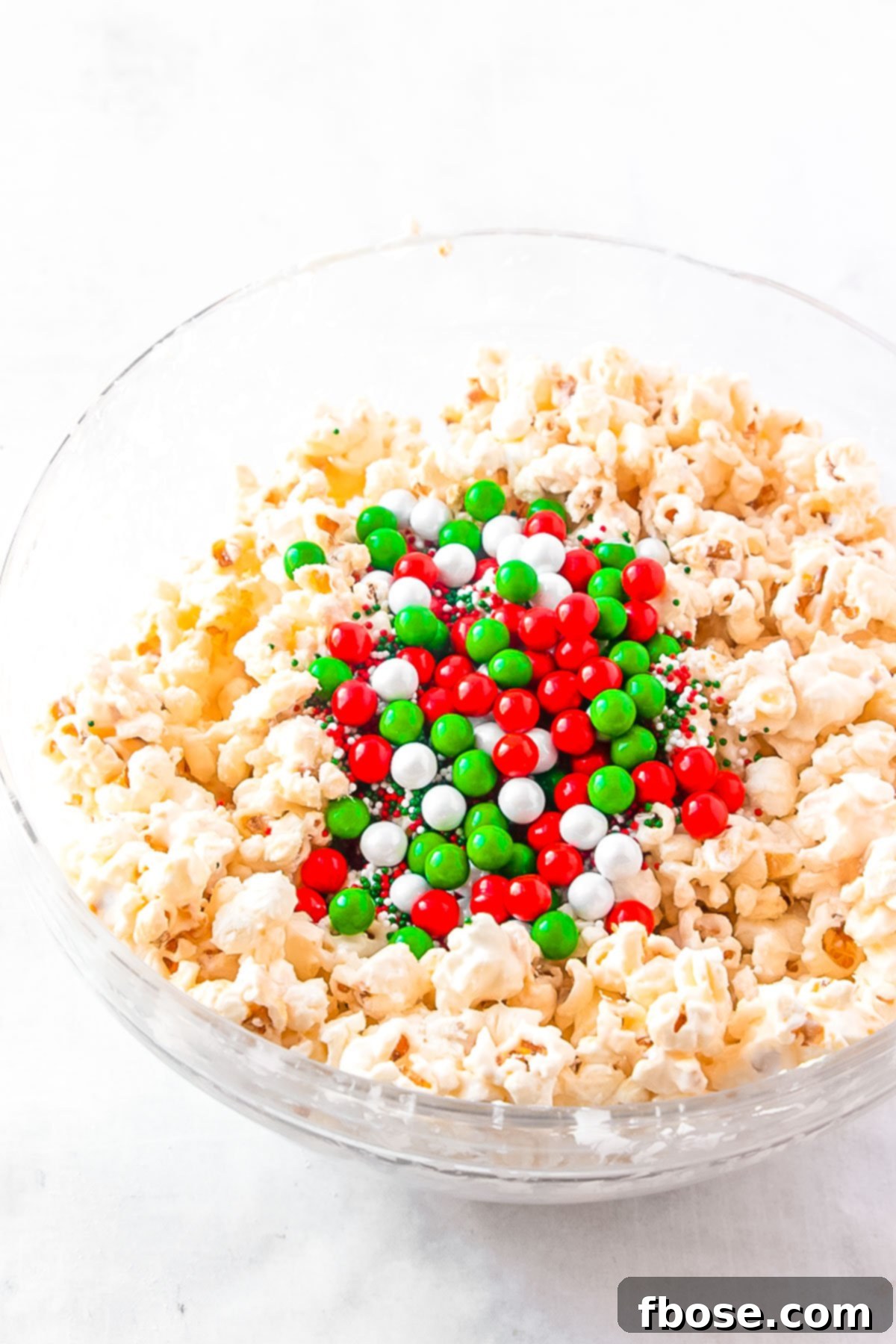 Candy and popcorn coated in white chocolate in a glass mixing bowl, just before spreading.