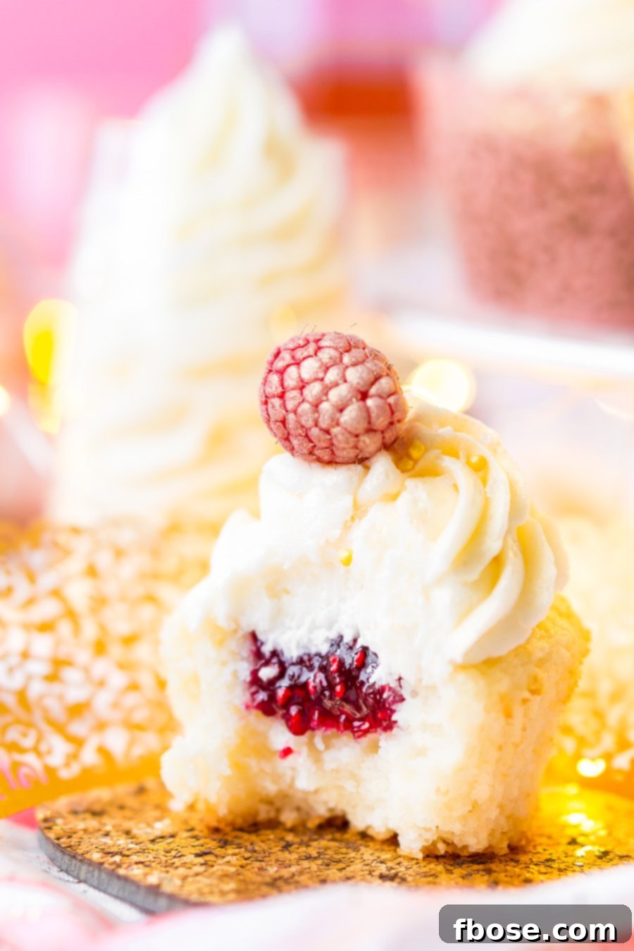 A beautifully composed shot of White Chocolate Raspberry Champagne Cupcakes, highlighting the delicate texture of the cake and the smooth, swirl of champagne buttercream. Perfect for any special occasion.
