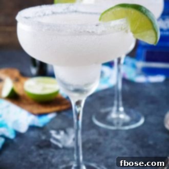 A vibrant, slushy frozen champagne margarita in a glass with a lime wedge garnish.