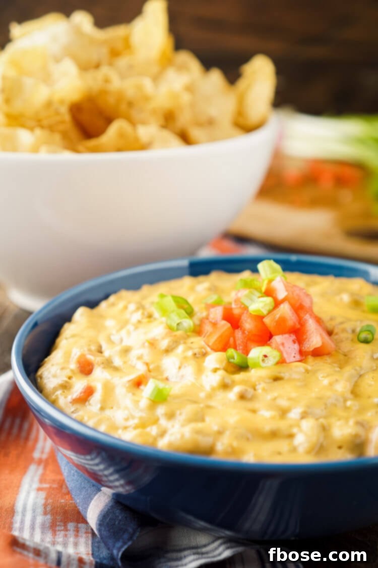 Close-up of the gooey, melted cheese and ground beef in a Cheeseburger Dip, garnished with fresh diced tomatoes and green onions, served with crispy tortilla chips.