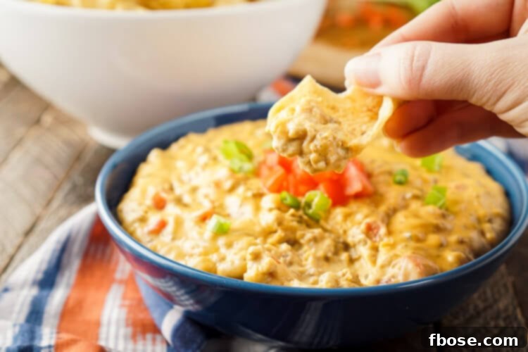 Overhead shot of Cheeseburger Dip, showcasing its rich, golden-brown cheese topping and a hint of the ground beef and other fixings underneath, served with a variety of dippers.