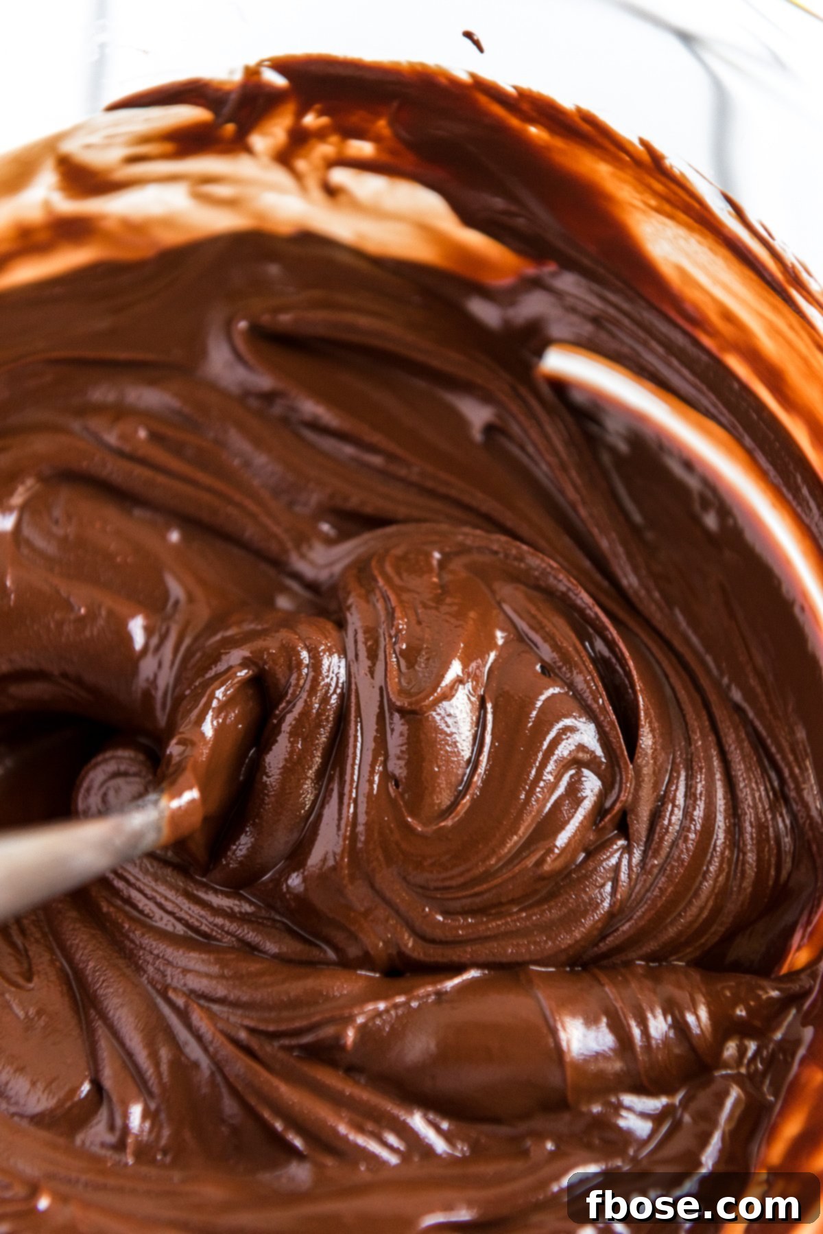 Fudgy Brownie Pie 5 Melted chocolate chips and butter being gently stirred in a glass bowl, creating a smooth and glossy ganache-like mixture.
