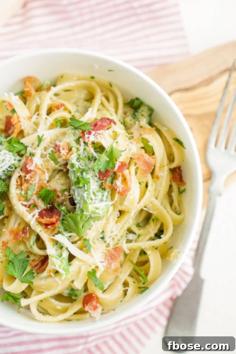 A close-up of a fork twirling Bacon and Broccoli Fettuccine Alfredo, showcasing the creamy sauce and pasta.