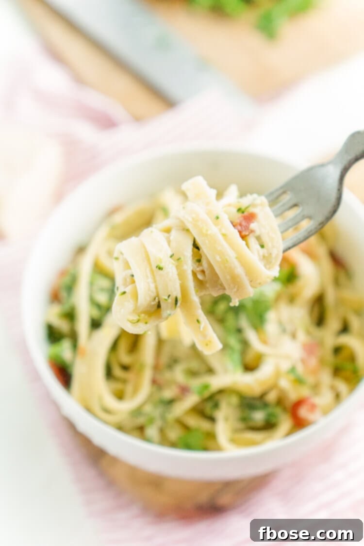 A large pot of Bacon and Broccoli Fettuccine Alfredo, ready to be served, with fresh parsley garnish.