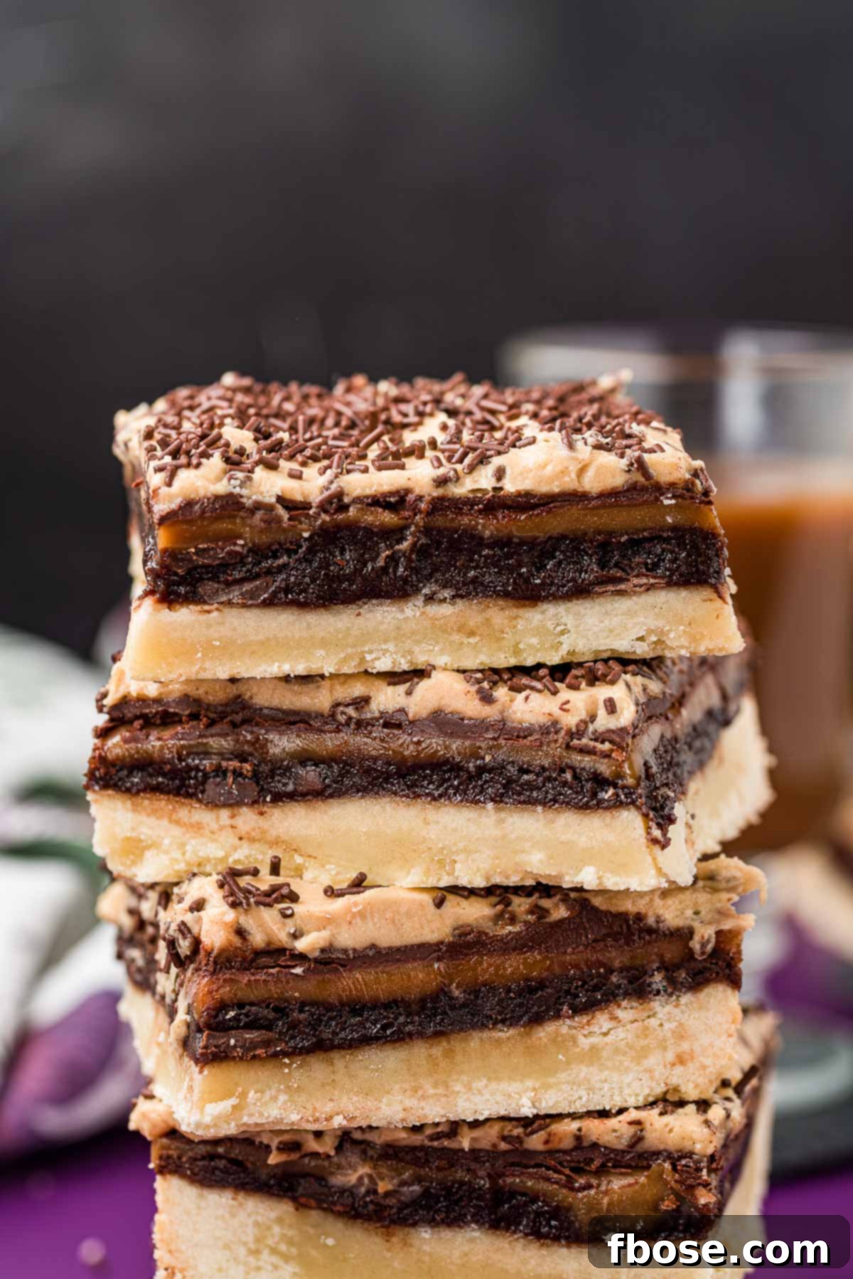 Golden Reserve Bars 2 A stack of four gourmet Billionaire Bars, showcasing their rich, multi-layered design with shortbread, brownie, caramel, chocolate, and peanut butter frosting.