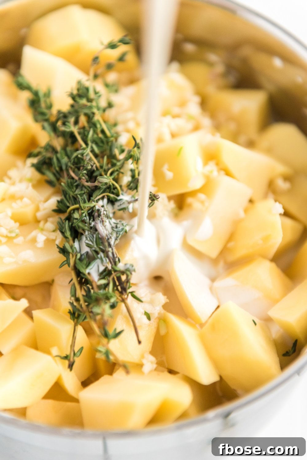 Milk being poured into pot with chopped potatoes, thyme, and garlic.