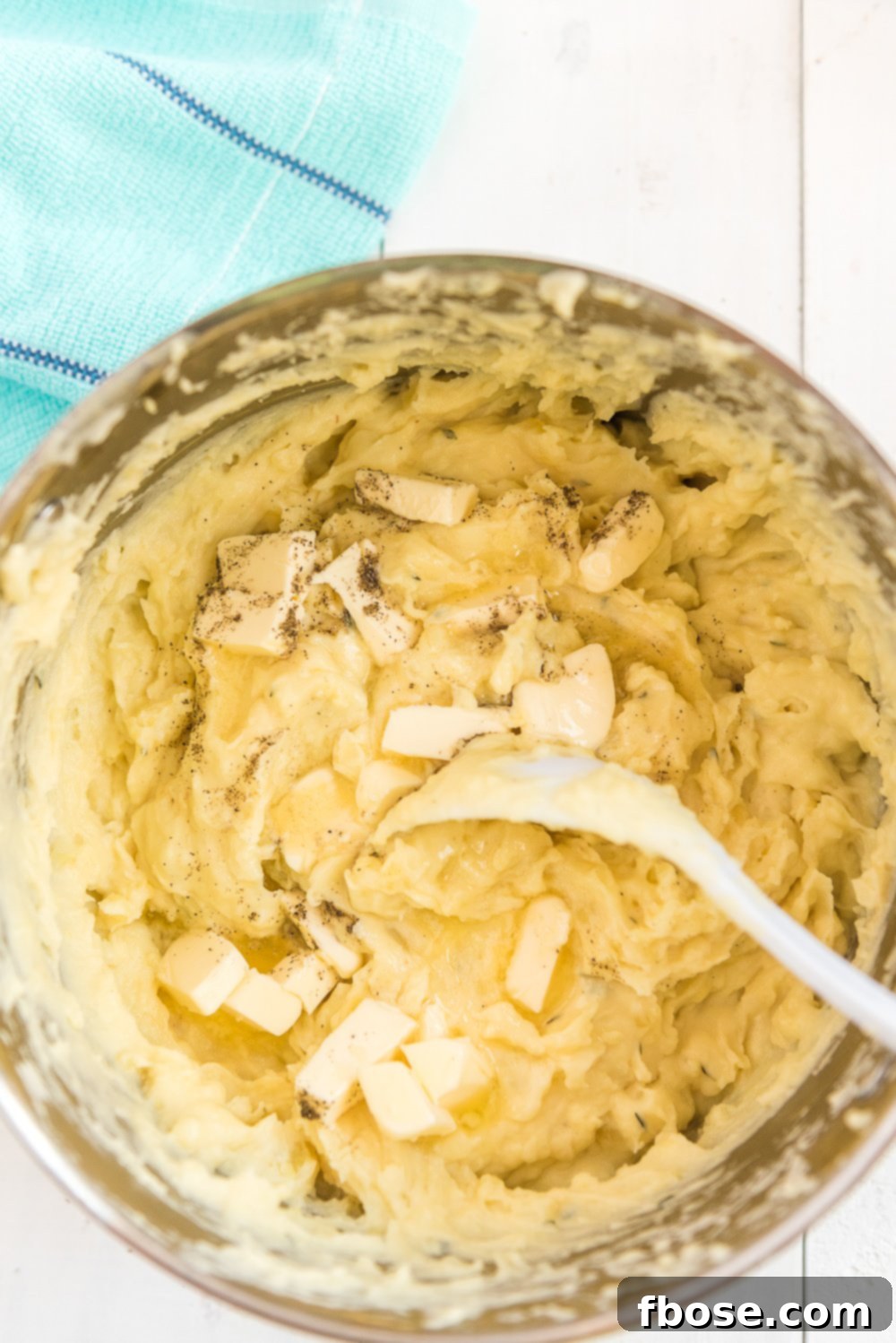 Overhead photo of butter, salt, and pepper being stirred into a pot of mashed potatoes.