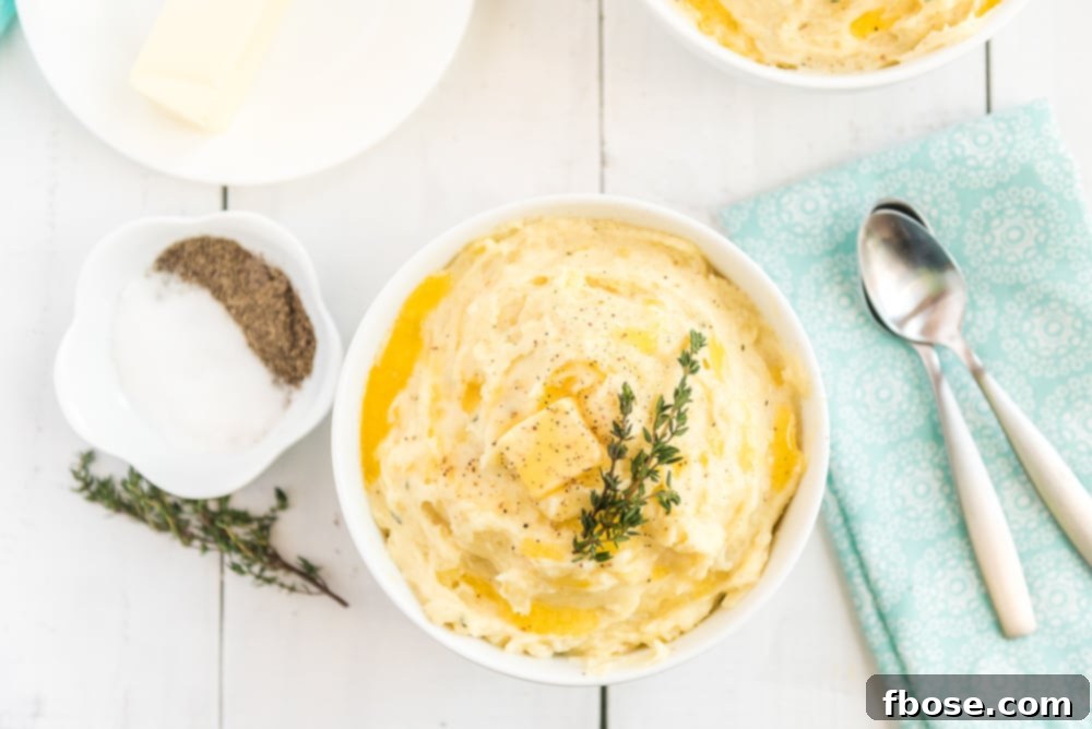 White bowl full of Creamy Garlic Mashed potatoes with salt, pepper and thyme.